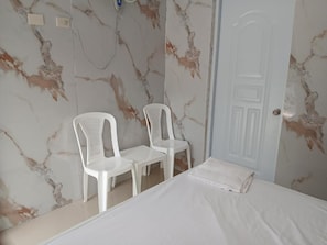 A bedroom with a bed, two white plastic chairs, a white door, and marble-patterned walls. - Paraíso Vacacional FERNANDO (Polo)