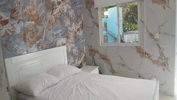 Un dormitorio con cama, mesita de noche, ventana y pared con diseño tipo mármol.