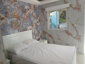 A bedroom with a bed, a nightstand, a window, and a wall with a marble-like pattern.
