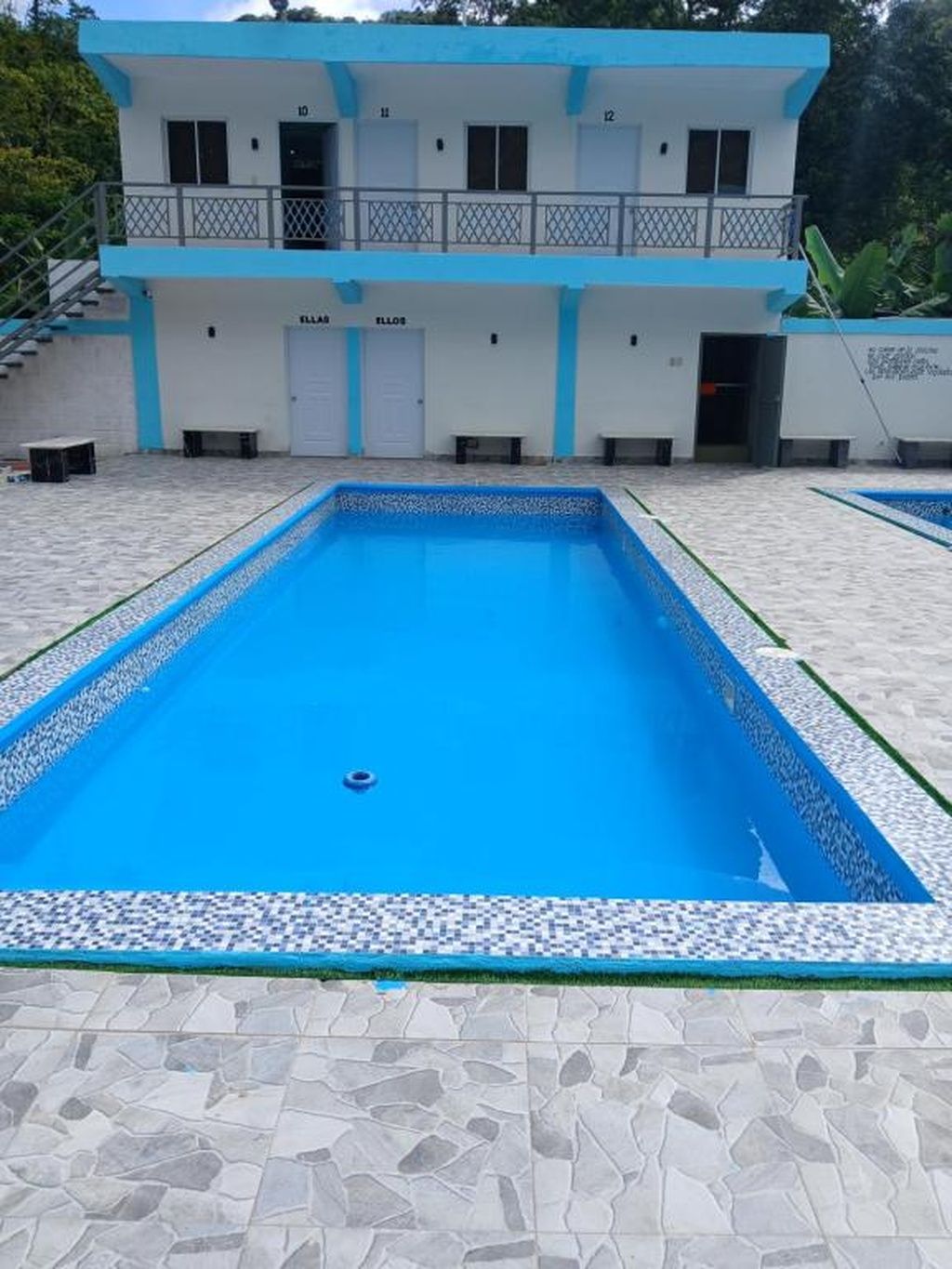 A rectangular swimming pool with a tiled edge, surrounded by a stone-tiled deck.