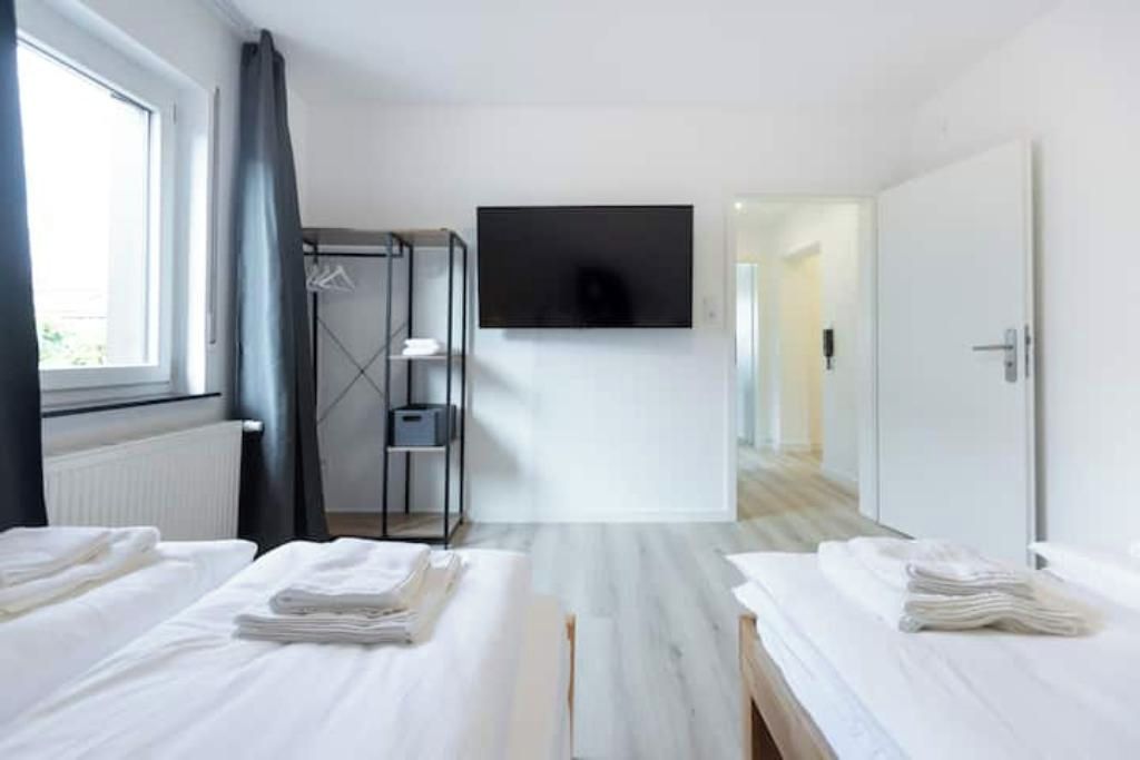 Une chambre d’hôtel avec deux lits, un téléviseur fixé au mur, une armoire et une vue sur le couloir.