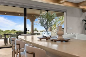 A modern dining area with a long table, chairs, and a decorative plant centerpiece. - Mangrove Estate - Brand New High End Home! (Anna Maria)