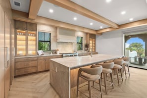 A modern kitchen with a large island, bar stools, and a view of the outdoors. - Mangrove Estate - Brand New High End Home! (Anna Maria)