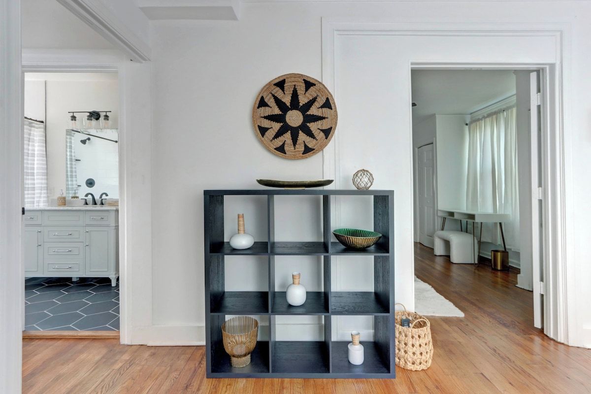 A modern interior with a black shelving unit, a decorative wall piece, and a view into a bathroom.