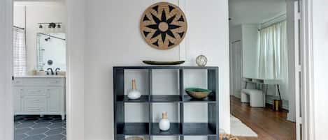 A modern interior with a black shelving unit, a decorative wall piece, and a view into a bathroom.