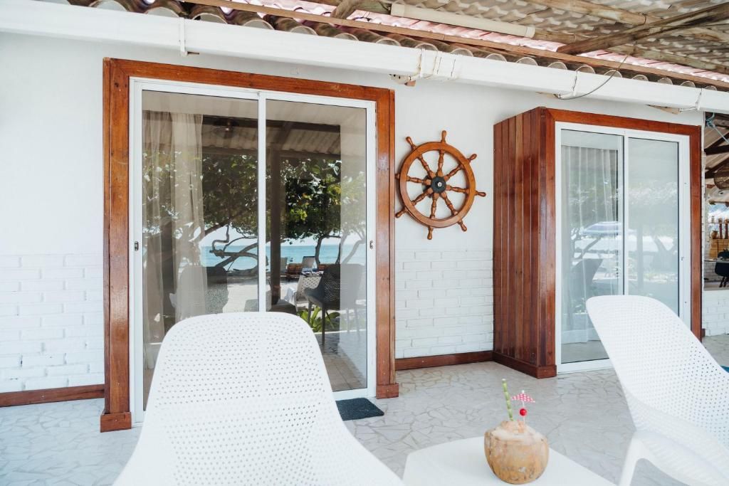 Un área de estar al aire libre techada, con un timón de madera decorativo, una puerta de vidrio que da a una piscina y una silla blanca.