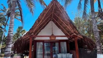 Una construcción con techo de paja, un área de estar cubierta y vista a la playa.