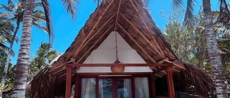 Una construcción con techo de paja, un área de estar cubierta y vista a la playa.