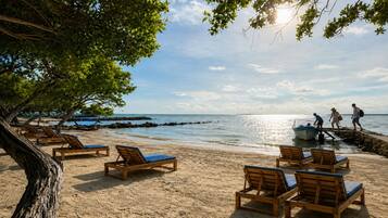 A beach with wooden lounge chairs and a rocky shoreline.