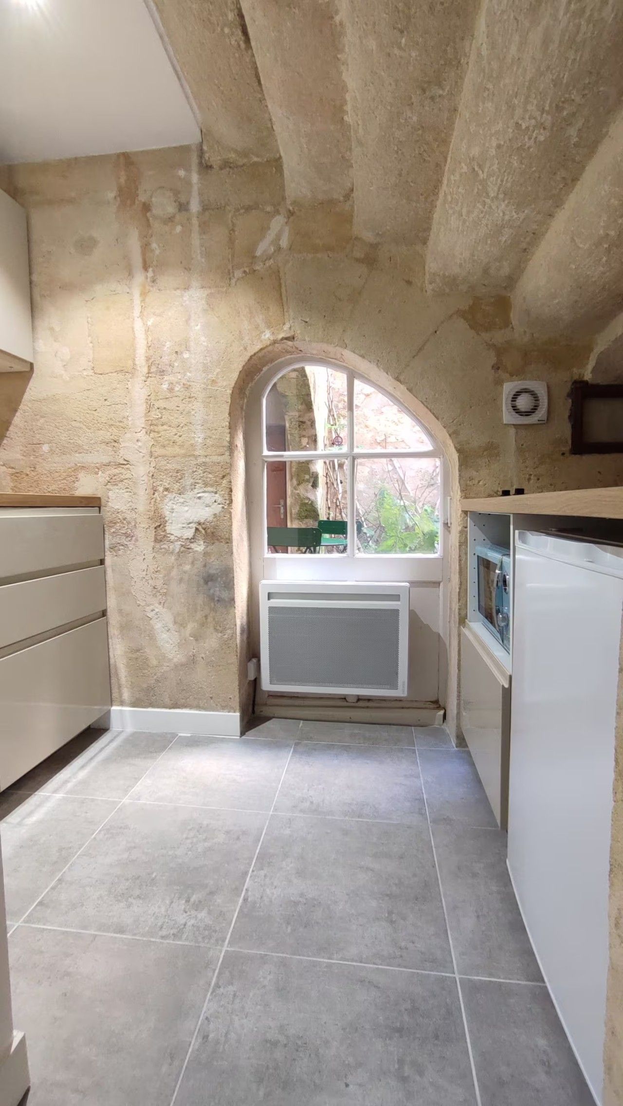 A kitchen with a stone wall, a window, and a built-in air conditioner.