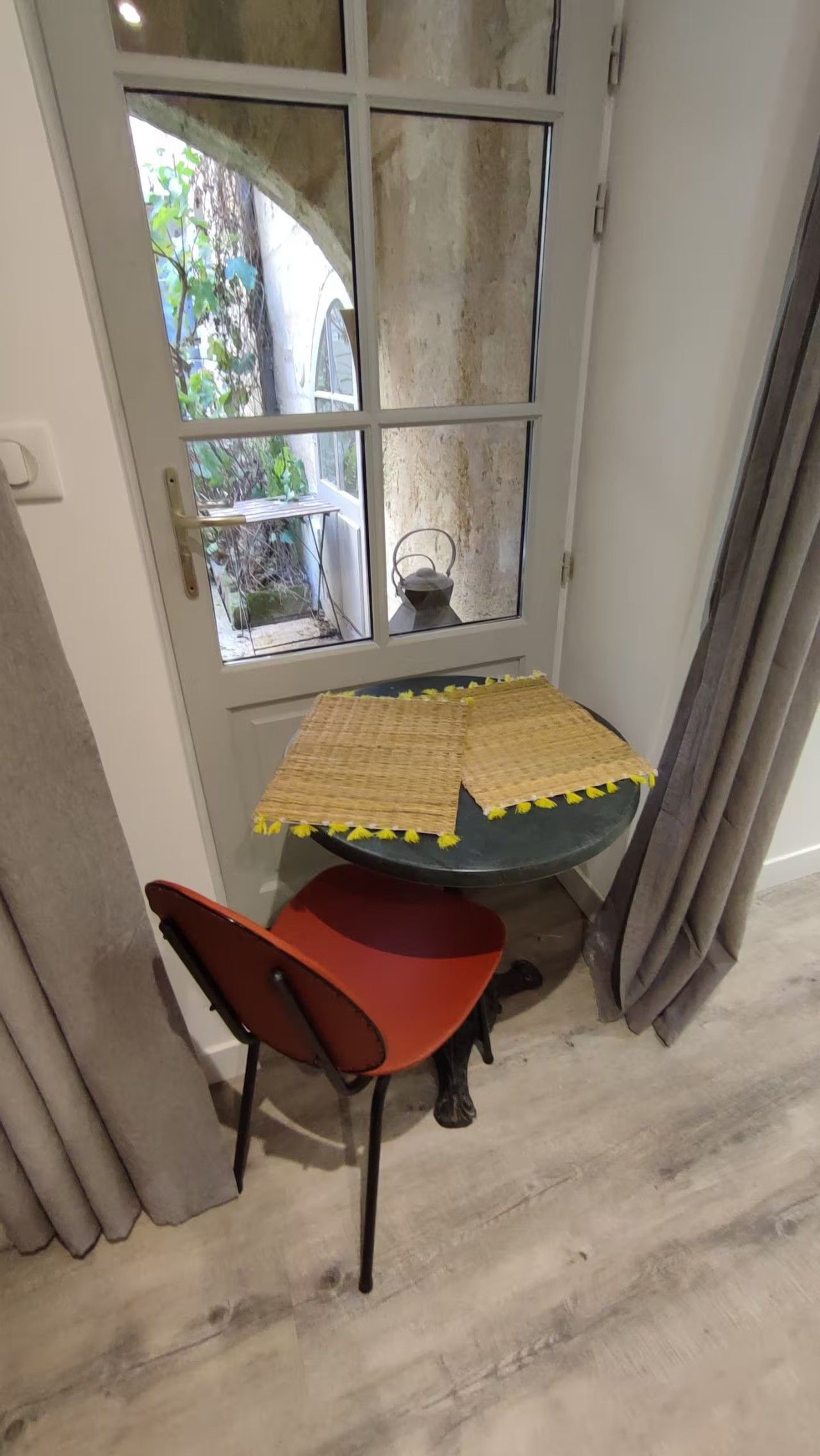 A corner room with a table and a chair, a window with a view of the outside, and a door.