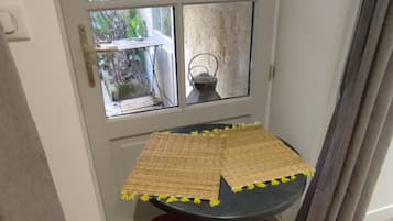 A corner room with a table and a chair, a window with a view of the outside, and a door.