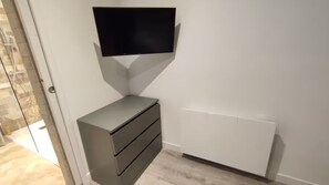 A corner room with a flat-screen TV mounted on the wall, a built-in cabinet with drawers, and a radiator. - Studio on patio in Chartrons (Bordeaux)