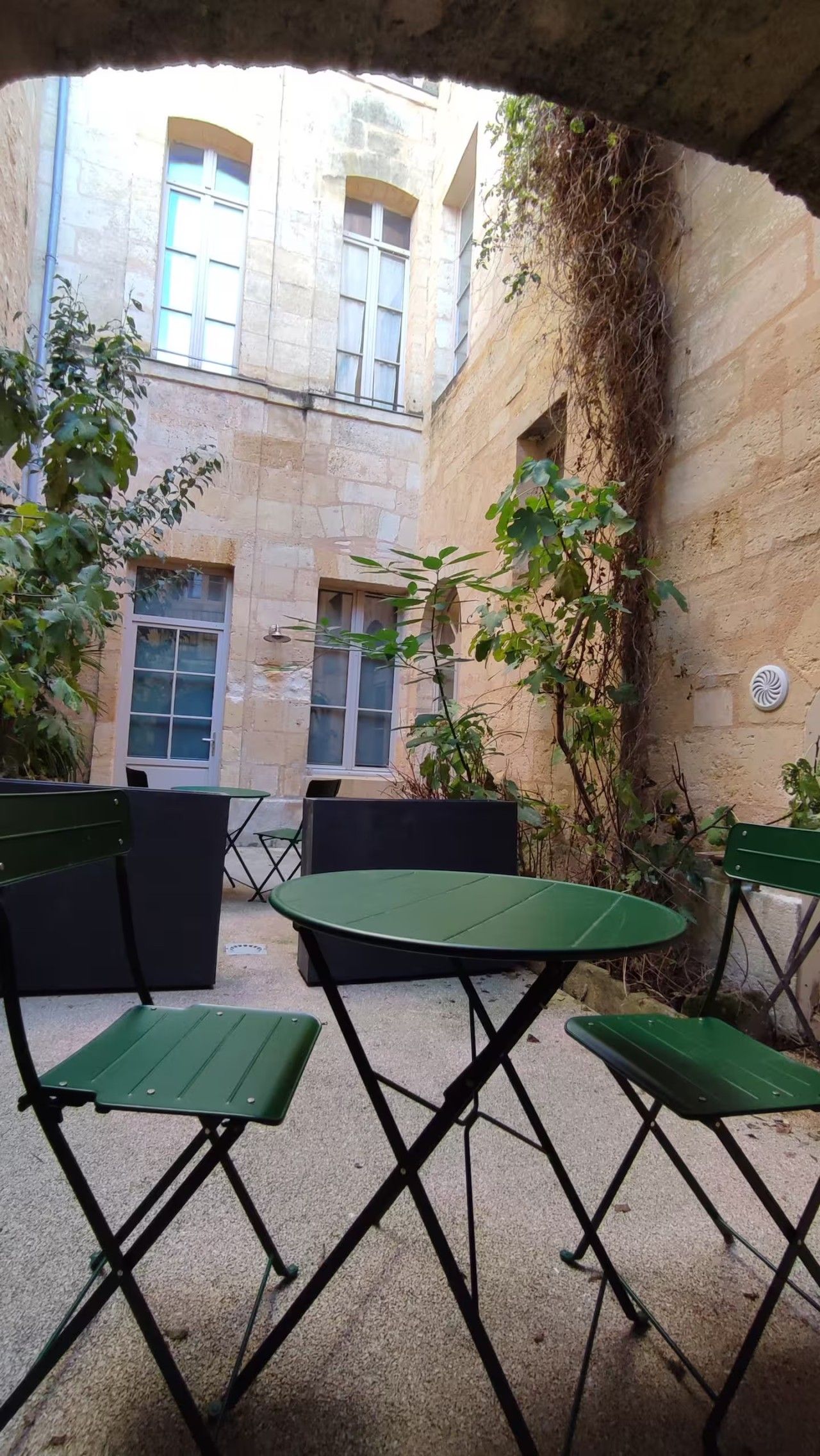 An outdoor seating area with a table and chairs, surrounded by stone walls and vegetation.