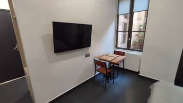 Una stanza piccola con TV a schermo piatto fissata al muro, un tavolo di legno con sedie e una finestra vista esterna.