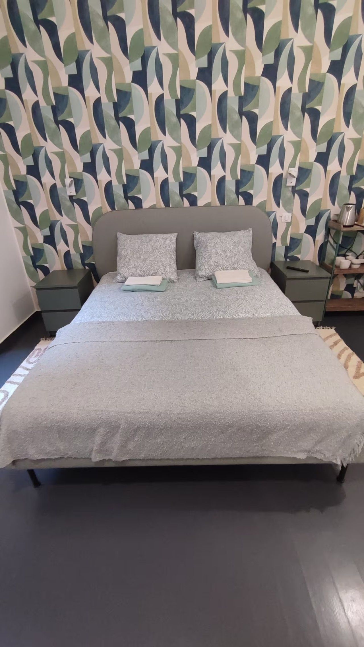A bed with a grey bedspread, two pillows, and a headboard against a wall with a geometric pattern.