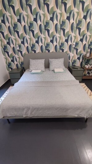 Un letto con copripiumino grigio, due cuscini e una testiera a muro con motivo geometrico.