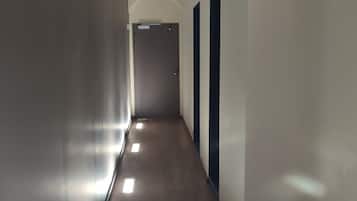 A long, narrow hallway with a wooden floor and white walls, leading to a door at the end.
