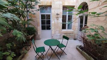 Patio esterno con tavolo rotondo e due sedie, circondato da pareti in pietra e vegetazione.
