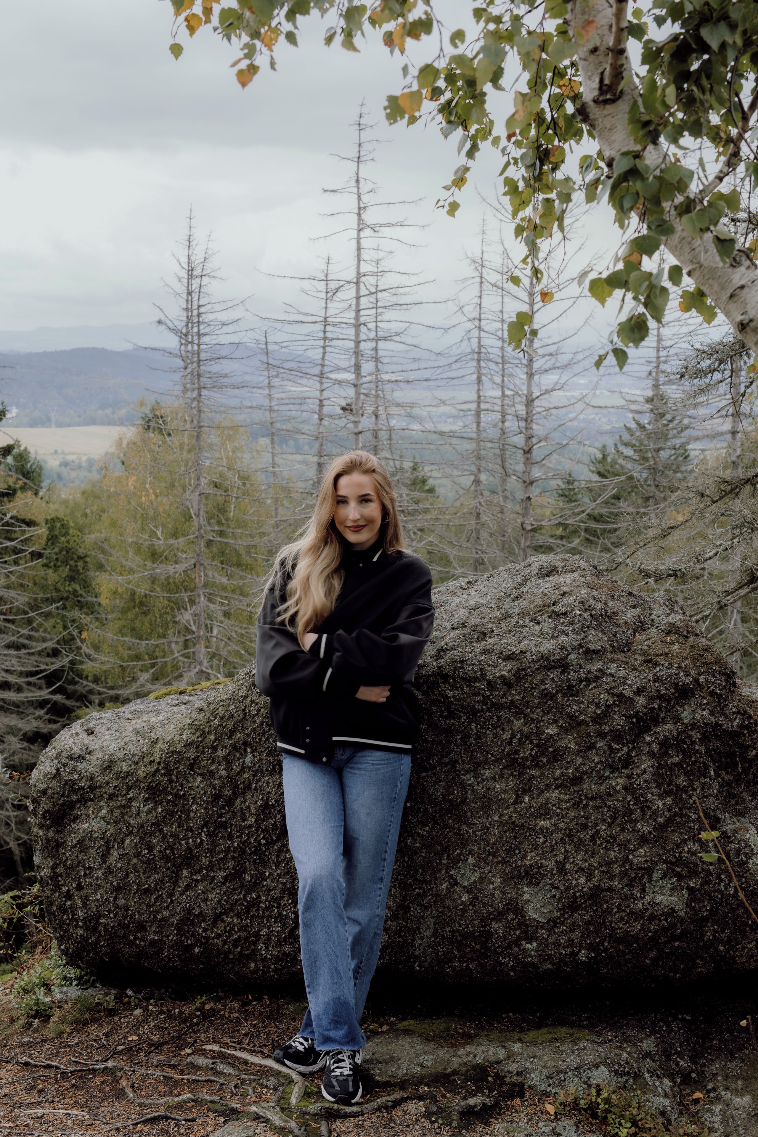 Eine Person steht in einer natürlichen Umgebung mit Bäumen und einem Berg im Hintergrund.