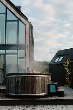 En modern byggnad med stora fönster och en utomhusbubbelpool i trä framför.