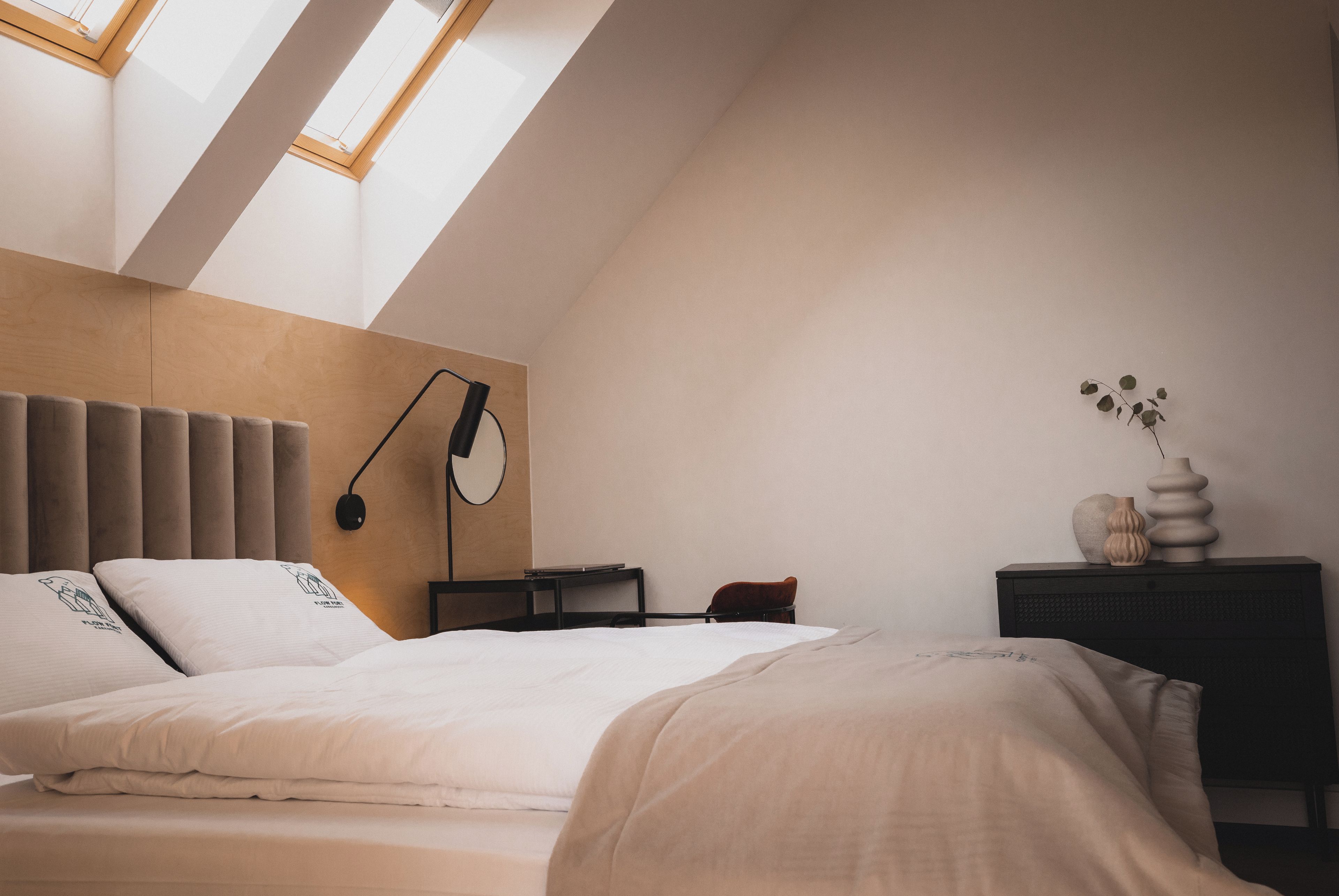 Une chambre avec un plafond en pente, un lit avec une literie blanche, une table de chevet avec une lampe et une petite plante posée sur la table de chevet.