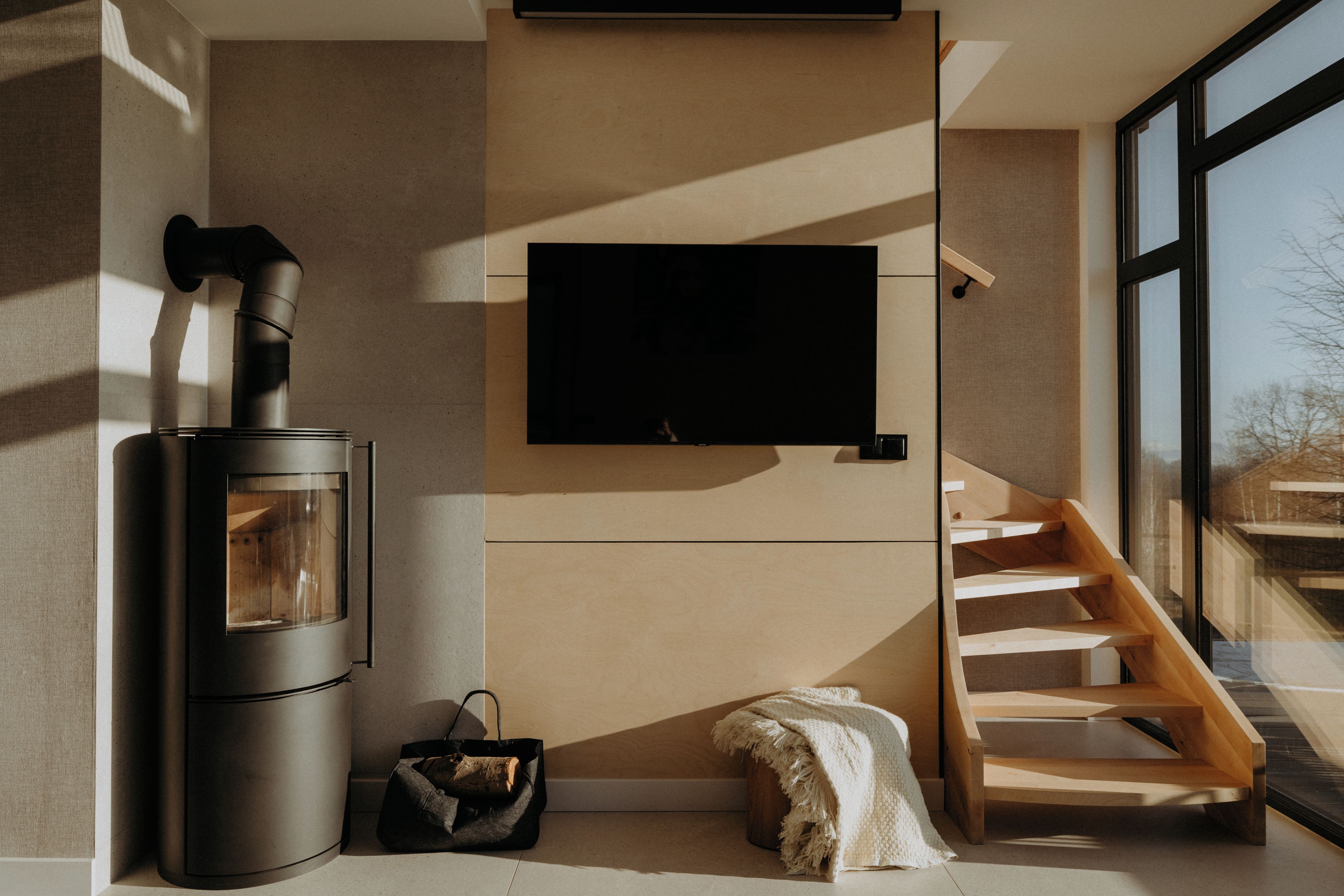 A modern interior with a wood-burning stove, a flat-screen TV mounted on a wall, and a wooden staircase.