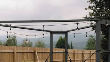Uma rede sob uma pérgola decorada com luzes, uma cerca de madeira e um gramado.