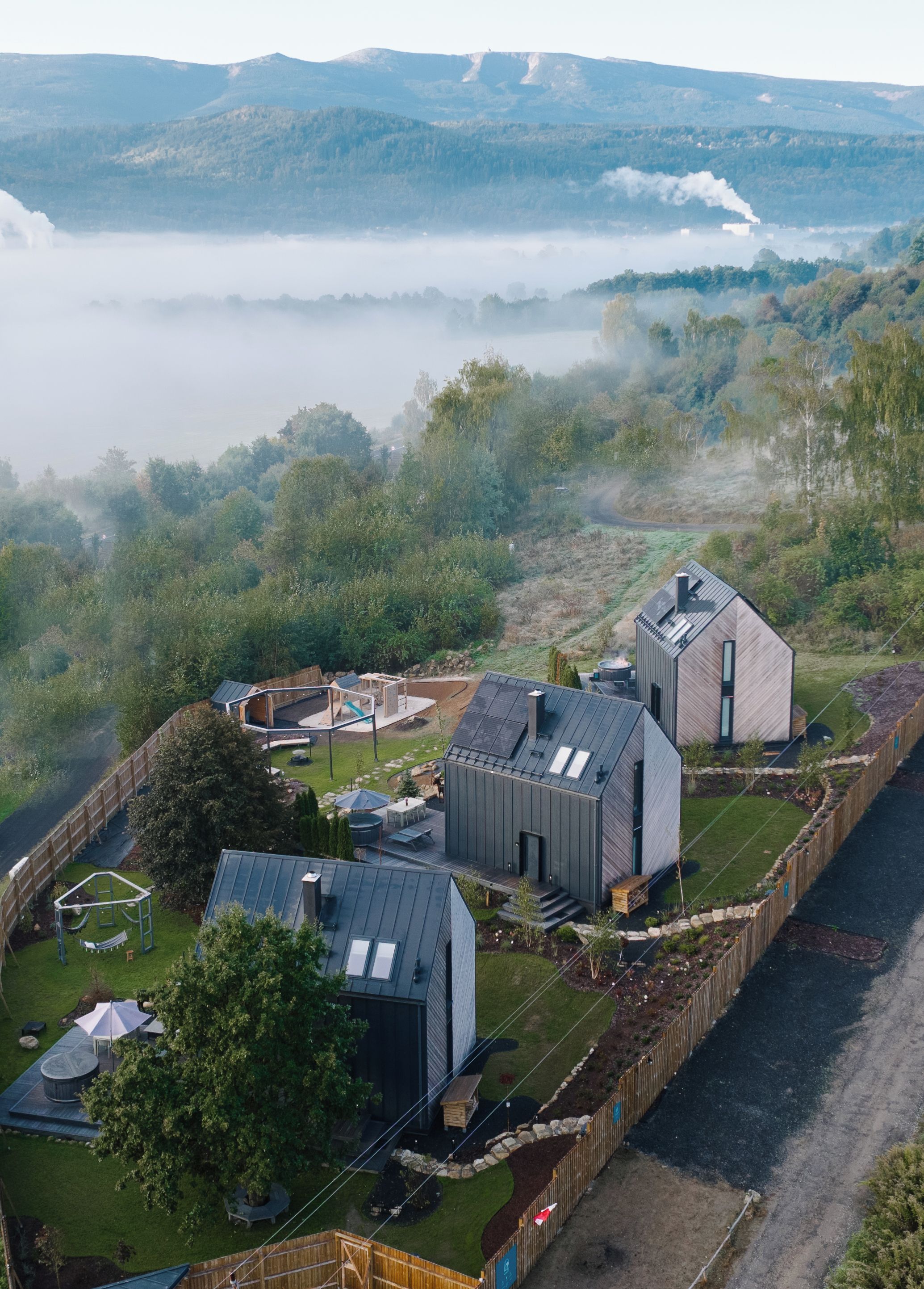 Een modern huis met een groot terras, een zwembad en uitzicht op een meer en bergen.