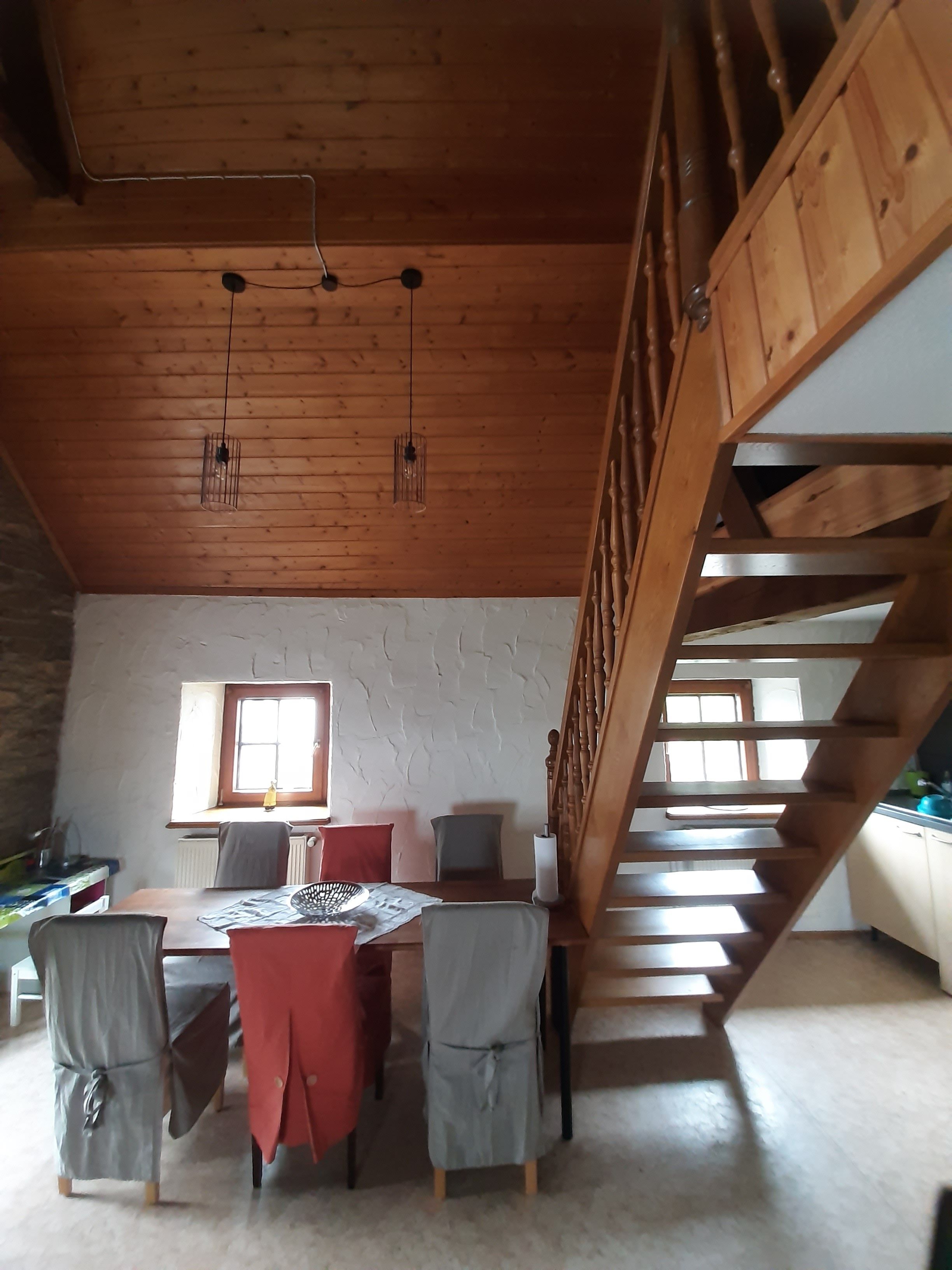 Ein Zimmer mit einer Holztreppe, einem Esstisch mit Stühlen und einem Fenster.
