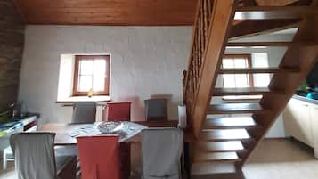 Ein Zimmer mit einer Holztreppe, einem Esstisch mit Stühlen und einem Fenster.