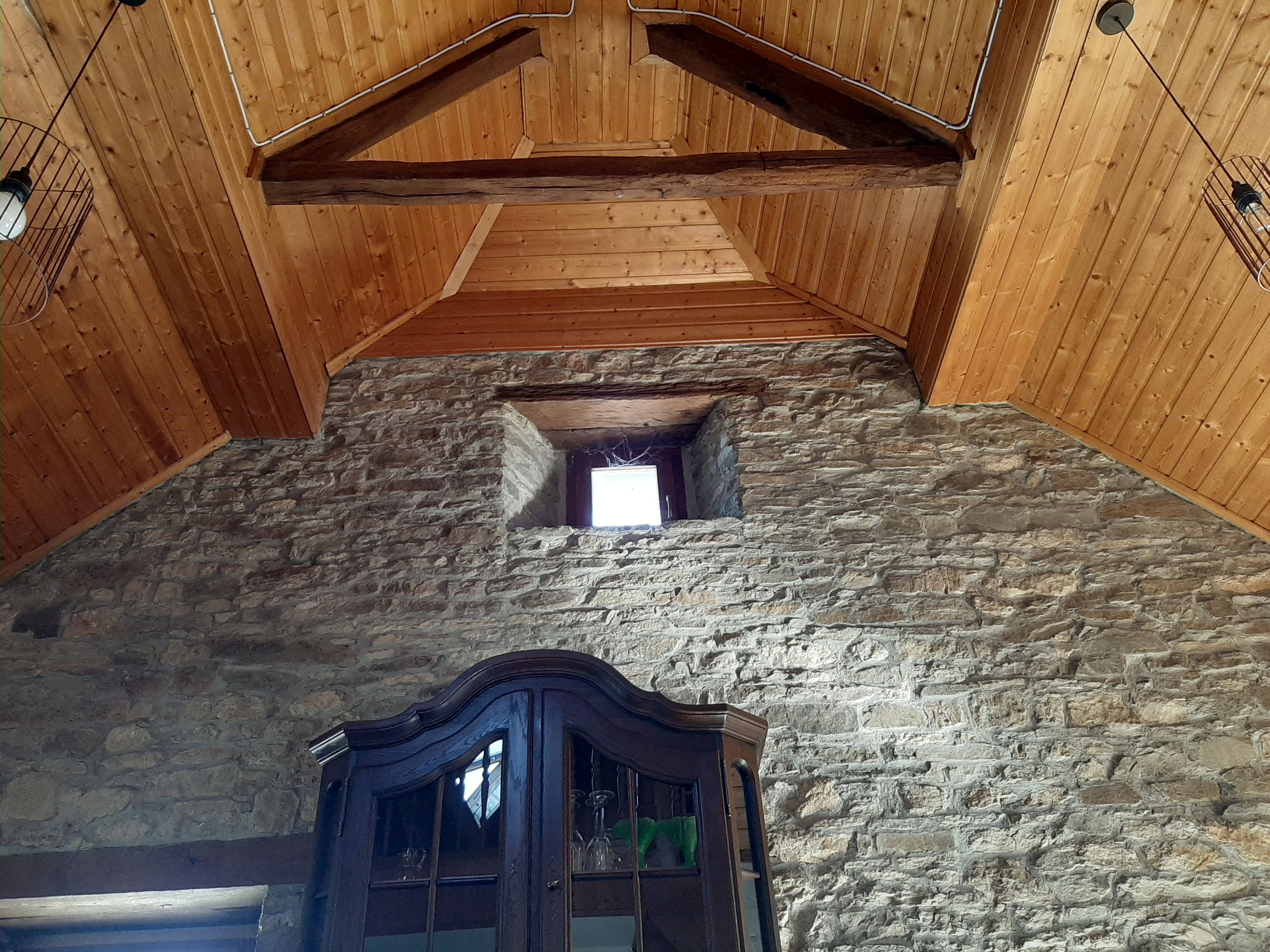 Ein Zimmer mit einer Steinwand, einer Holzbalkendecke und einem kleinen Fenster.