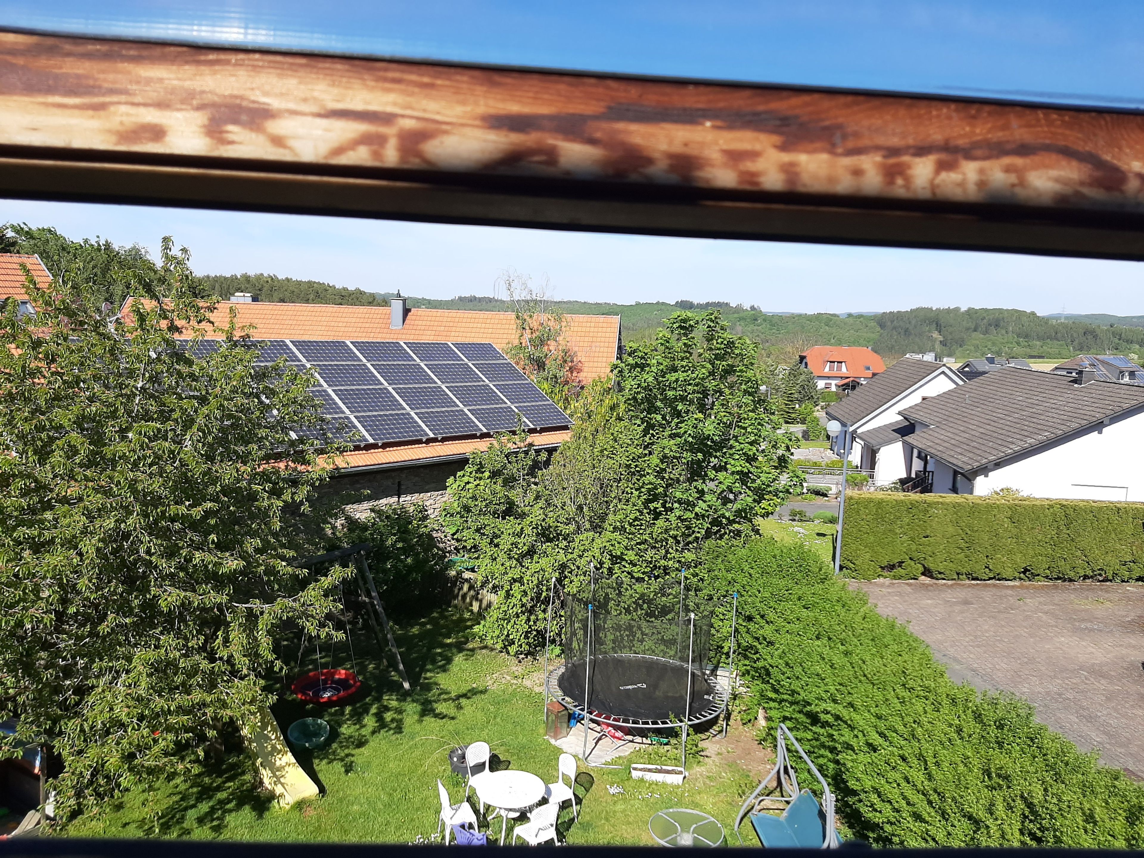 Ein Wohngebiet mit Solaranlage auf einem Hausdach, einem Trampolin im Garten und freiem Blick auf die umliegende Nachbarschaft.