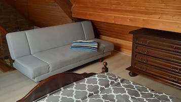 Ein Schlafzimmer im Loft-Stil mit schrägem Dach, einem grauen Sofa, einer Holzkommode und einer Betttdecke mit Muster.