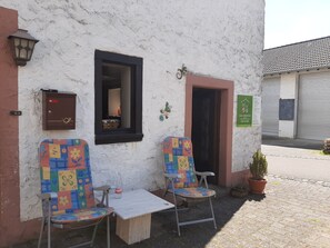 An outdoor seating area with two chairs and a table, a wall-mounted light, and a door with a window.