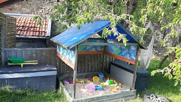 Ein kleines Spielhäuschen mit einem bunten Dach und einer Sandkiste voller Spielzeug.