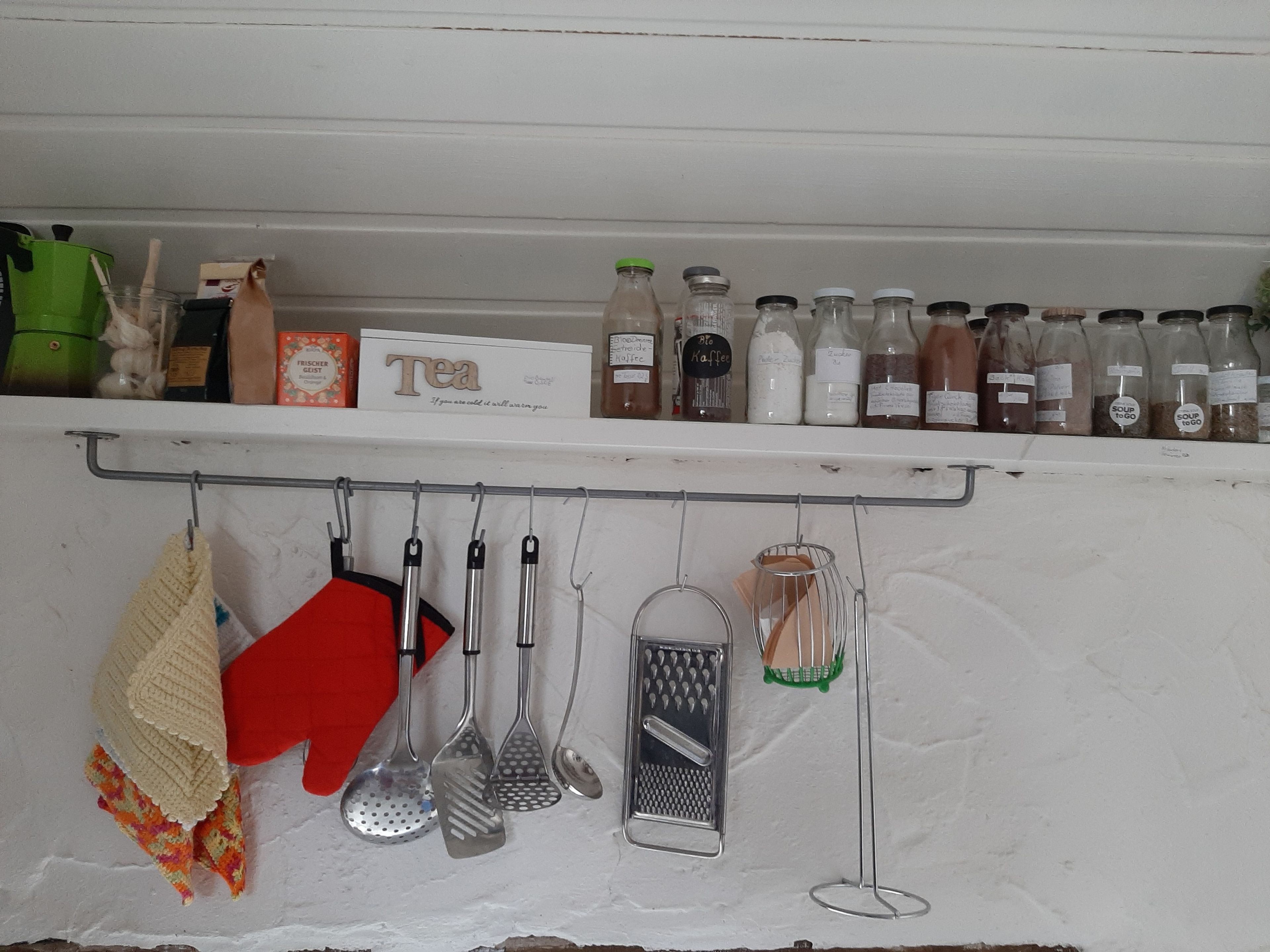 A kitchen shelf with various kitchen utensils and bottles of tea and coffee.