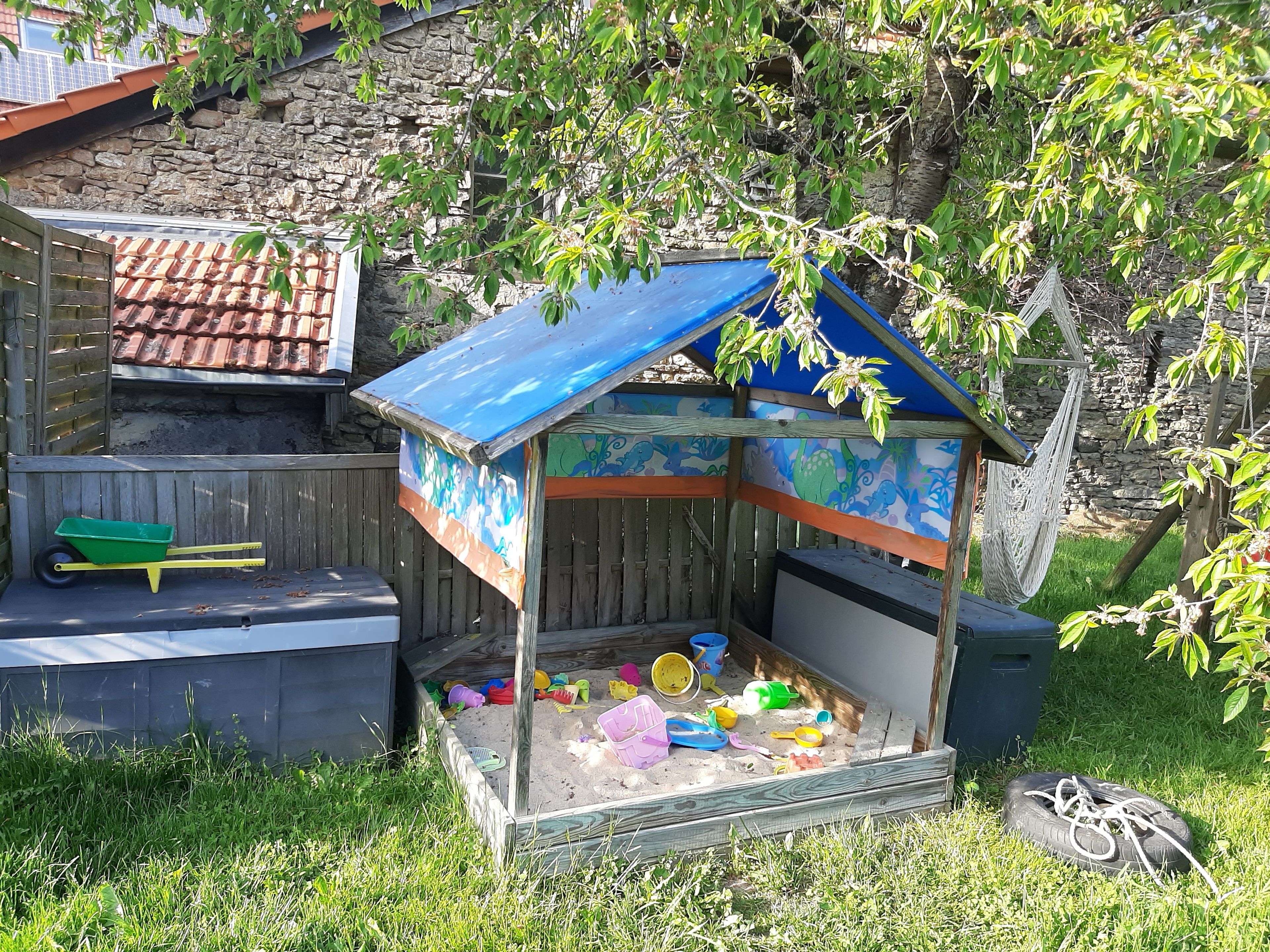 Ein kleines Spielhäuschen mit einem bunten Dach und einer Sandkiste voller Spielzeug.