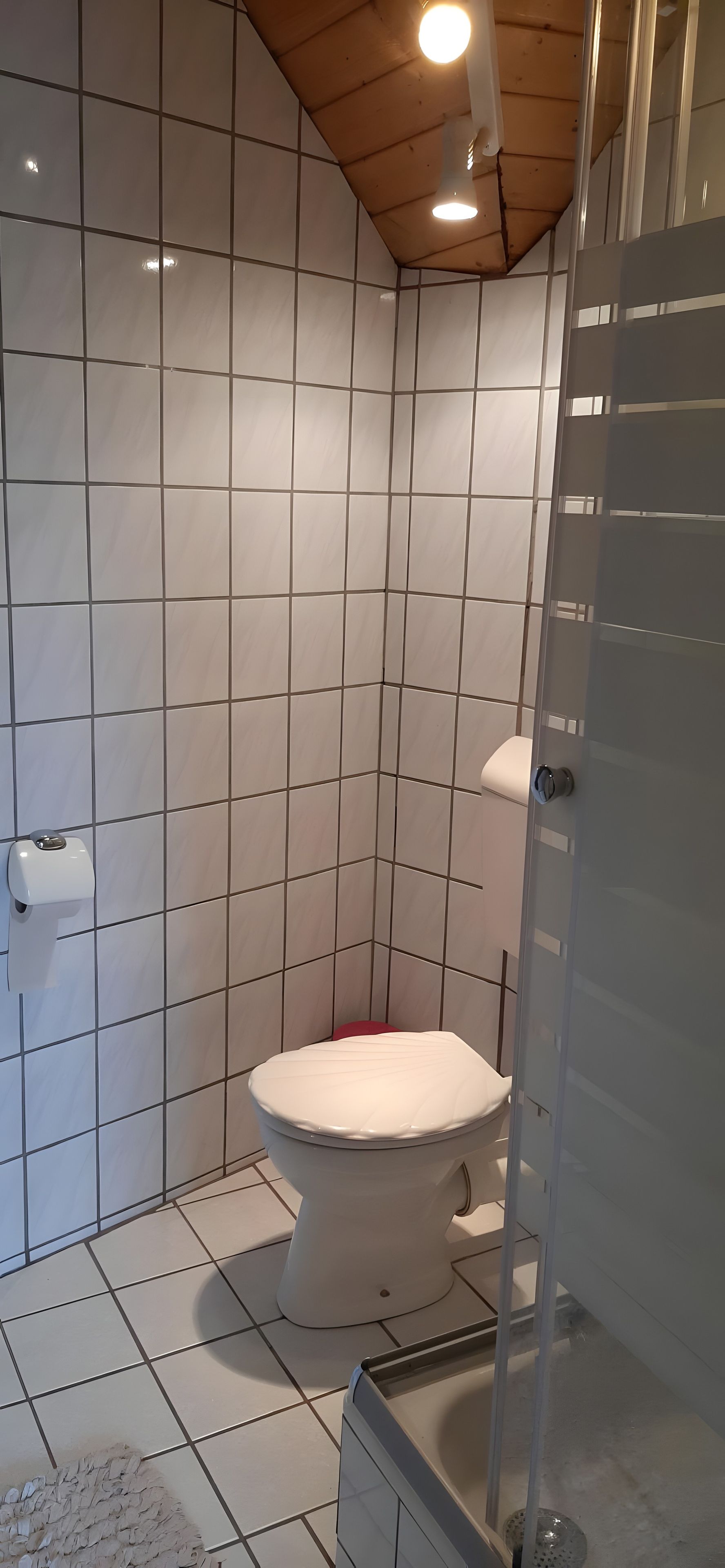 Kylpyhuone, jossa on wc, käsienkuivaaja ja lasiseinäinen suihkutila.