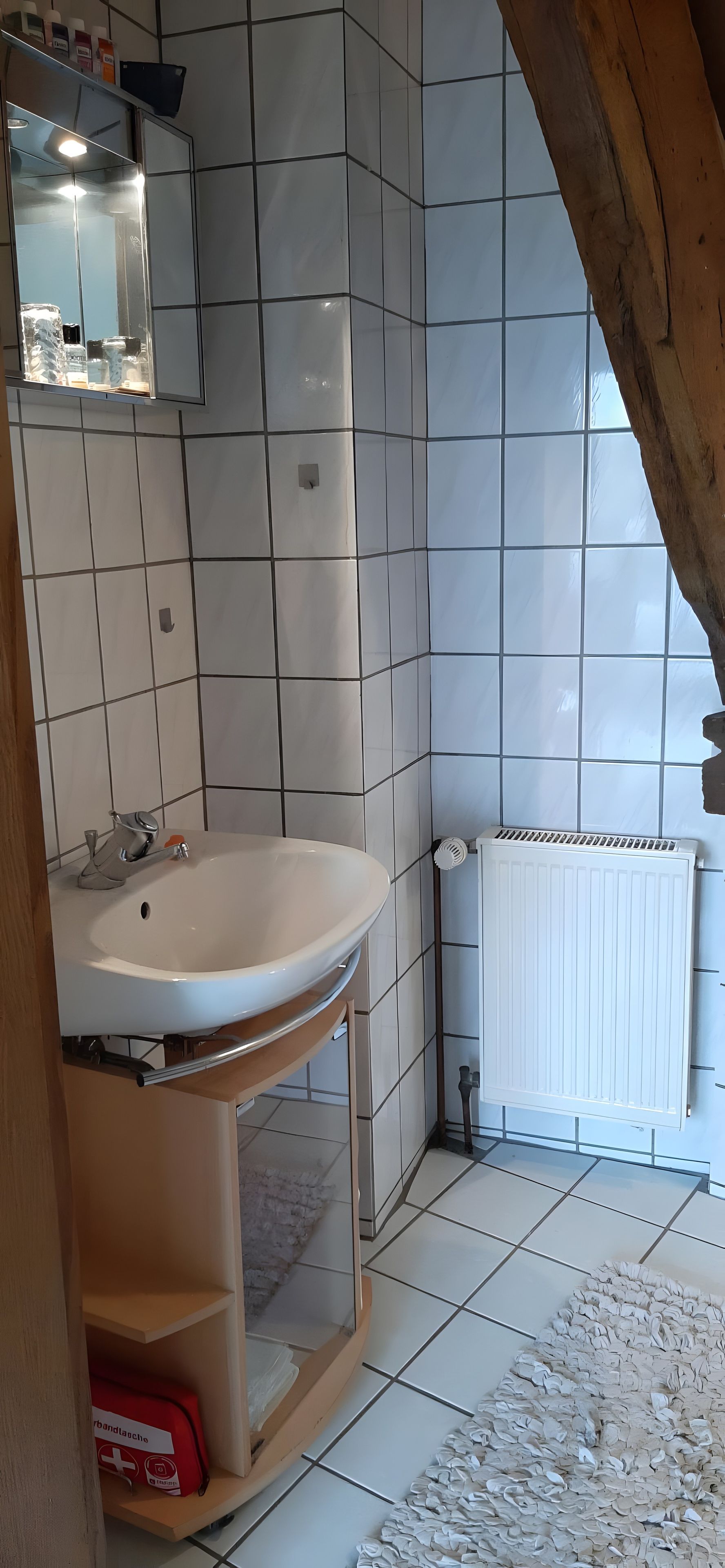 A bathroom with a white sink, tiled walls, a radiator, and a wooden ceiling beam.
