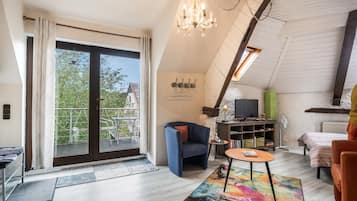 A spacious living room with a large sliding glass door leading to a balcony, a chandelier, a television, and a cozy seating area.
