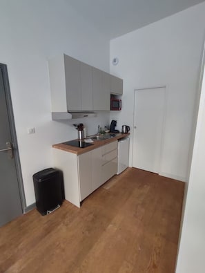 A compact kitchen with white cabinets, a microwave, a coffee maker, and a trash bin. - Apartment in the heart of the Chartrons (Bordeaux)