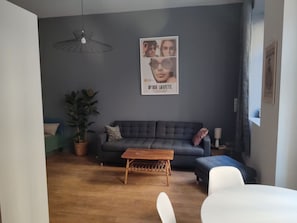 A living room with a dark grey sofa, a wooden coffee table, and a hanging light fixture. - Apartment in the heart of the Chartrons (Bordeaux)