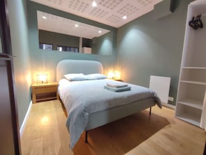 A bedroom with a bed, bedside lamps, a nightstand, and a white shelving unit. - Apartment in the heart of the Chartrons (Bordeaux)