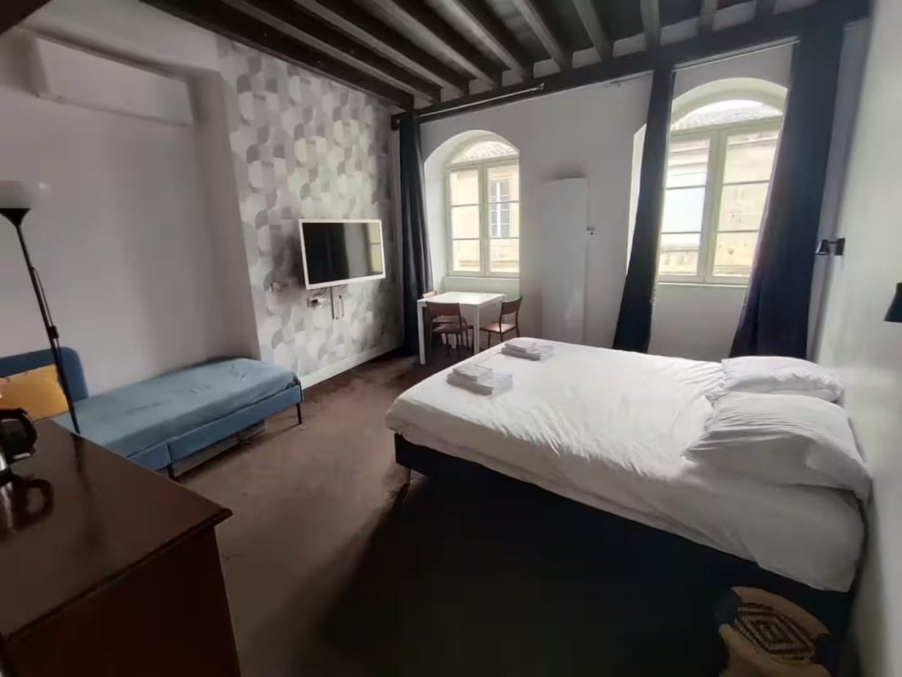 A hotel room with a bed, a desk, a chair, and a TV.