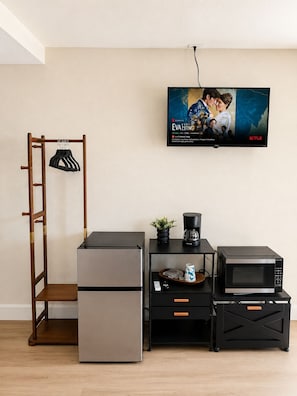 A kitchenette with a refrigerator, microwave, coffee maker, and a TV displaying a movie poster.