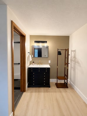 A bathroom with a double vanity, a mirror with lights, a towel rack, and a wooden rack. - Kiva Motel Mountain Retreat (Show Low)