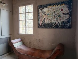 Una stanza con una grande finestra, una panca in pelle marrone e un quadro astratto dai colori vivaci appeso alla parete.