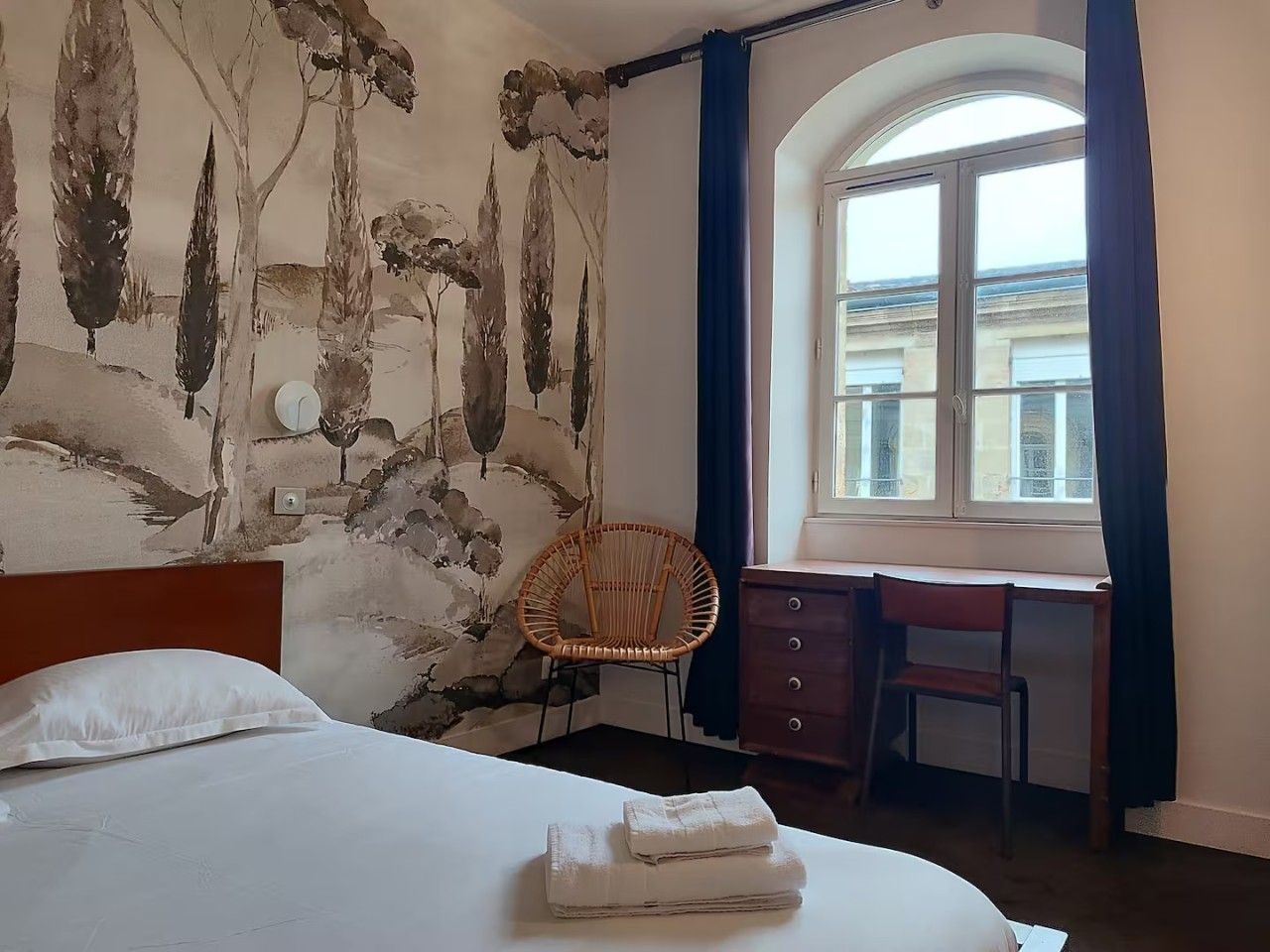 A hotel room with a bed, a desk, a chair, and a window with curtains.