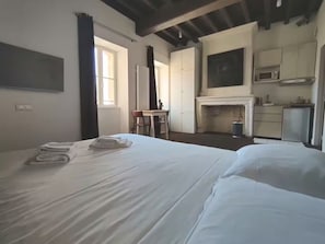 A hotel room with a large bed, a desk, a chair, and a kitchenette. - Quiet Courtyard Apartment in Chartrons with Air Conditioning (Bordeaux)